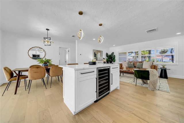 8001 13th Ave S, Saint Petersburg, FL 33707 - kitchen with wine cooler, light wood-style floors, white cabinetry, a textured ceiling, and pendant lighting