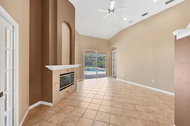 12342 Lavender Loop, Bradenton, FL 34212 - unfurnished living room featuring a ceiling fan, a tiled fireplace, light tile patterned floors, high vaulted ceiling, and arched walkways