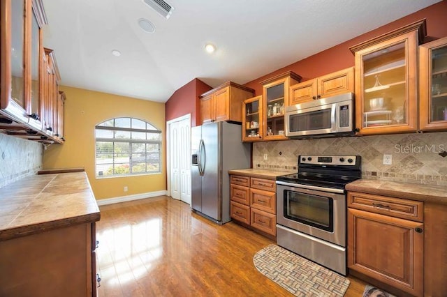 4127 Middle River Ter, Ellenton, FL 34222 - kitchen with stainless steel appliances, vaulted ceiling, glass insert cabinets, light wood-style floors, and tasteful backsplash