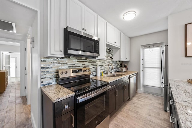 441 62nd St, Holmes Beach, FL 34217 - kitchen featuring stainless steel appliances, white cabinets, light wood finished floors, tasteful backsplash, and light stone counters