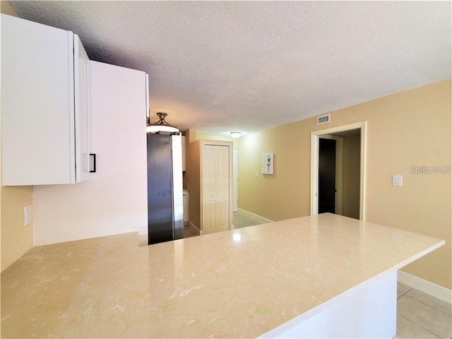 2763 Woodgate Ln Unit 105, Sarasota, FL 34231 - kitchen featuring a peninsula, a textured ceiling, white cabinets, and light tile patterned flooring