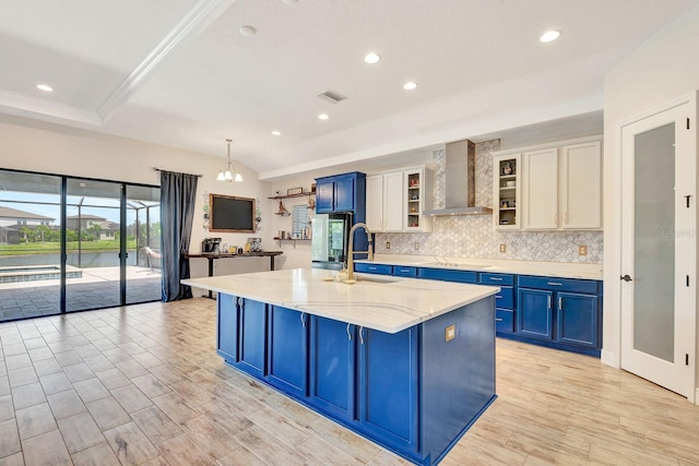 9215 Isabella Cir, Parrish, FL 34219 - kitchen featuring wall chimney range hood, blue cabinets, a kitchen island with sink, backsplash, and light wood-style floors
