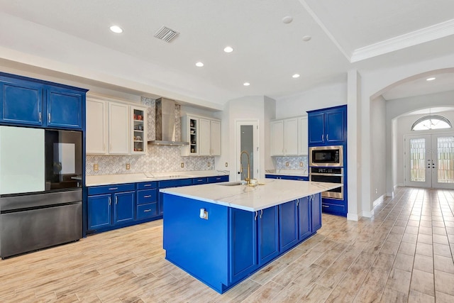 9215 Isabella Cir, Parrish, FL 34219 - kitchen with stainless steel appliances, wall chimney exhaust hood, blue cabinetry, arched walkways, and french doors