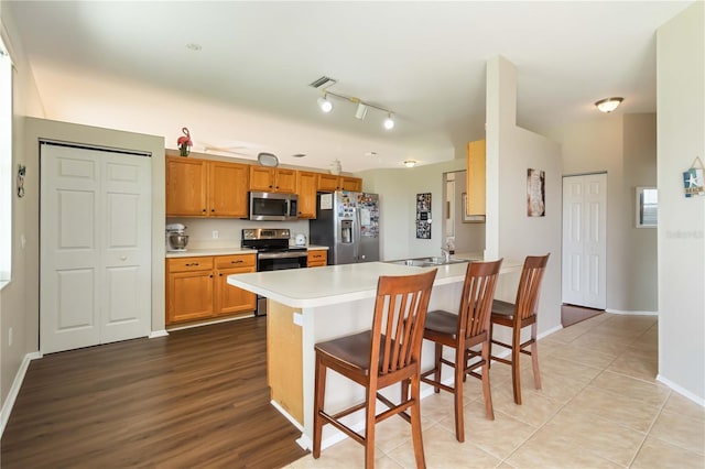 9410 71st Ave E, Palmetto, FL 34221 - kitchen with stainless steel appliances, a peninsula, light countertops, a kitchen bar, and brown cabinets