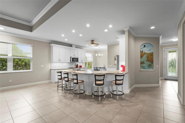18050 Wooden Skiff Ct, Nokomis, FL 34275 - kitchen featuring stainless steel microwave, plenty of natural light, a breakfast bar, light tile patterned floors, and crown molding