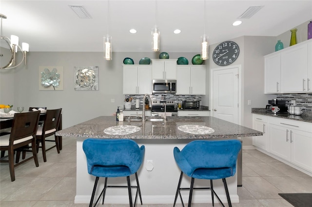 5134 Jackel Chase Dr, Wimauma, FL 33598 - kitchen featuring stainless steel microwave, tasteful backsplash, a kitchen bar, light tile patterned flooring, and recessed lighting