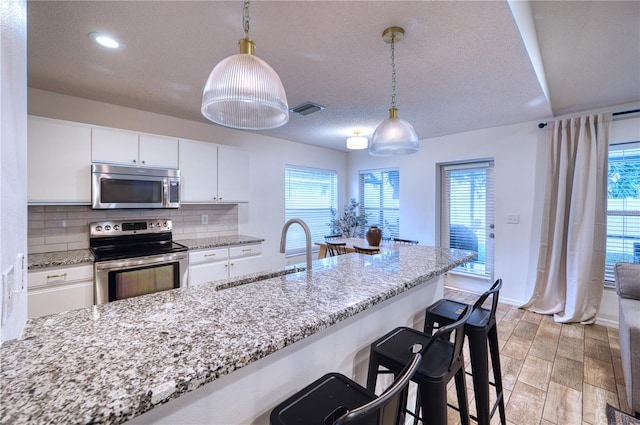 4204 Malickson Dr, Parrish, FL 34219 - kitchen with stainless steel appliances, backsplash, white cabinetry, a kitchen breakfast bar, and decorative light fixtures