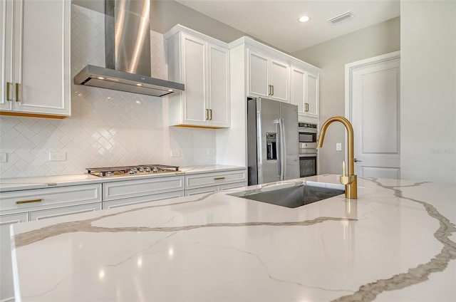 14312 Skipping Stone Loop, Parrish, FL 34219 - kitchen featuring wall chimney exhaust hood, stainless steel appliances, white cabinets, tasteful backsplash, and light stone countertops