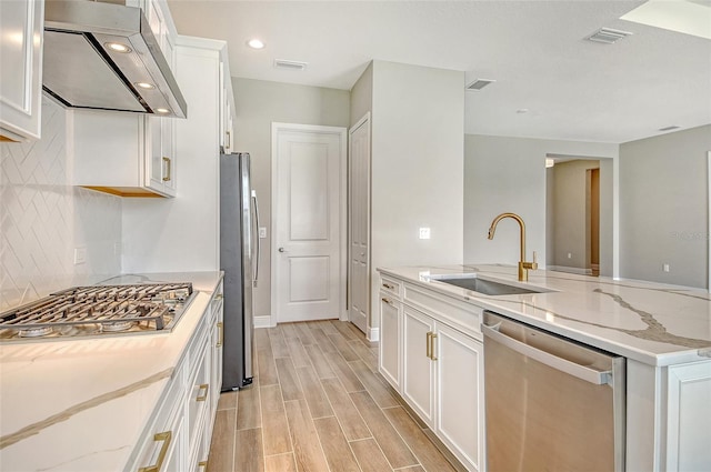 14312 Skipping Stone Loop, Parrish, FL 34219 - kitchen featuring stainless steel appliances, exhaust hood, white cabinets, tasteful backsplash, and light stone counters