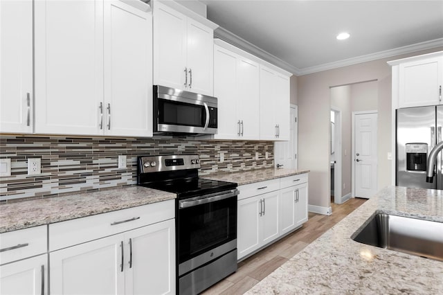 5174 78th St Cir E, Bradenton, FL 34203 - kitchen with appliances with stainless steel finishes, white cabinetry, decorative backsplash, light wood-style flooring, and ornamental molding