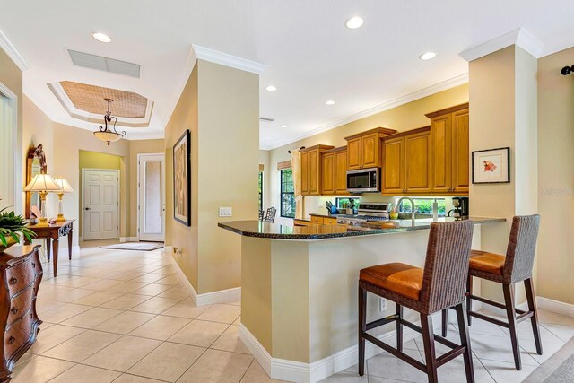 7314 Wexford Ct, Lakewood Ranch, FL 34202 - kitchen with stainless steel appliances, brown cabinetry, dark stone countertops, crown molding, and a kitchen breakfast bar