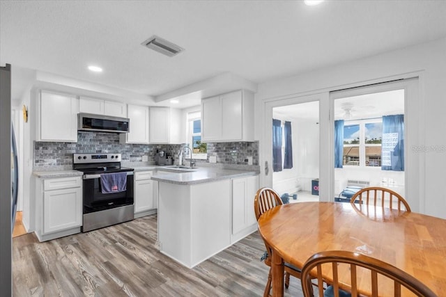 5401 Mac Arthur Ave, New Port Richey, FL 34652 - kitchen featuring stainless steel appliances, light wood-style flooring, white cabinets, light countertops, and backsplash