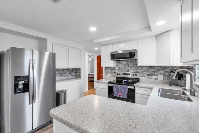 5401 Mac Arthur Ave, New Port Richey, FL 34652 - kitchen featuring appliances with stainless steel finishes, a peninsula, backsplash, white cabinets, and a textured ceiling