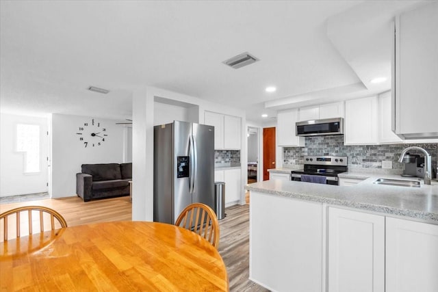 5401 Mac Arthur Ave, New Port Richey, FL 34652 - kitchen with stainless steel appliances, light wood-style floors, decorative backsplash, white cabinets, and recessed lighting
