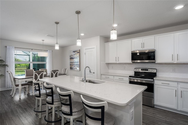 9144 Royal River Cir, Parrish, FL 34219 - kitchen featuring appliances with stainless steel finishes, a center island with sink, dark wood-style flooring, tasteful backsplash, and white cabinets