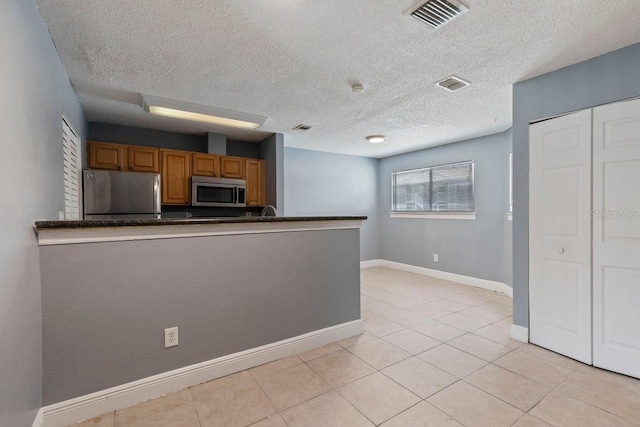 7298 Ulmerton Rd Unit 202, Largo, FL 33771 - kitchen with stainless steel appliances, brown cabinetry, light tile patterned flooring, a textured ceiling, and a peninsula