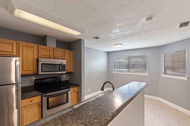 7298 Ulmerton Rd Unit 202, Largo, FL 33771 - kitchen featuring stainless steel appliances, dark countertops, a textured ceiling, light tile patterned floors, and brown cabinetry