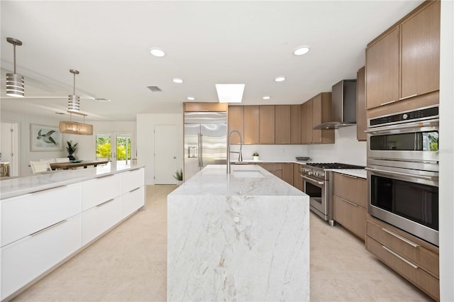311 Island Cir, Sarasota, FL 34242 - kitchen with high end appliances, wall chimney range hood, an island with sink, light stone countertops, and hanging light fixtures