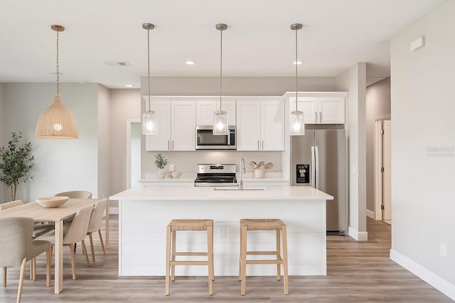 5534 Fairlane Dr, North Port, FL 34288 - kitchen with stainless steel appliances, light countertops, light wood-type flooring, white cabinetry, and a kitchen island with sink