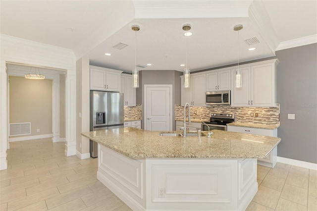 1226 Riverscape St, Bradenton, FL 34208 - kitchen featuring appliances with stainless steel finishes, a center island with sink, backsplash, light stone counters, and decorative light fixtures