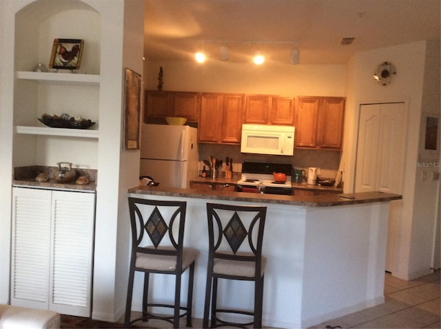 8397 38th Street Cir E Unit 305, Sarasota, FL 34243 - kitchen with white appliances, a breakfast bar area, light tile patterned floors, built in features, and brown cabinets