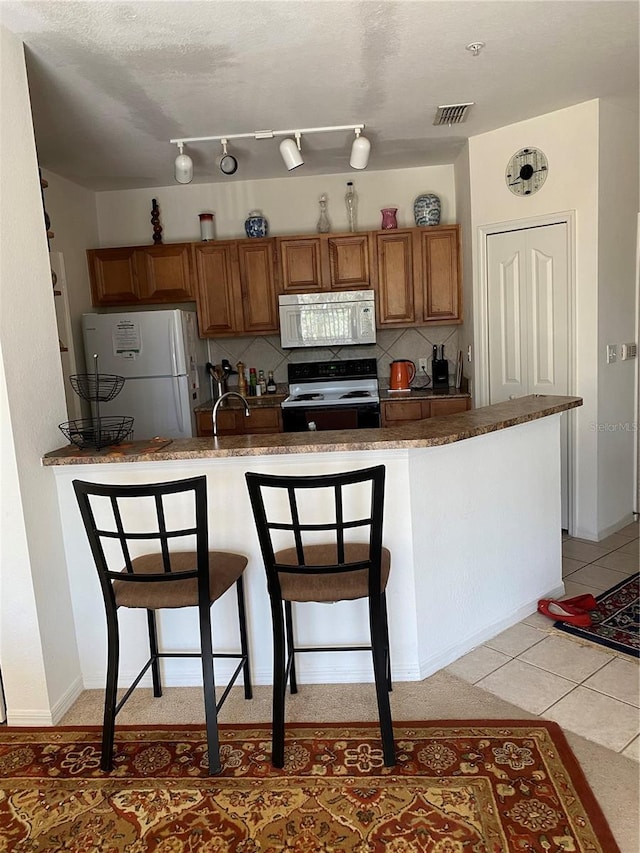 8397 38th Street Cir E Unit 305, Sarasota, FL 34243 - kitchen featuring white appliances, brown cabinets, decorative backsplash, a breakfast bar, and light tile patterned floors