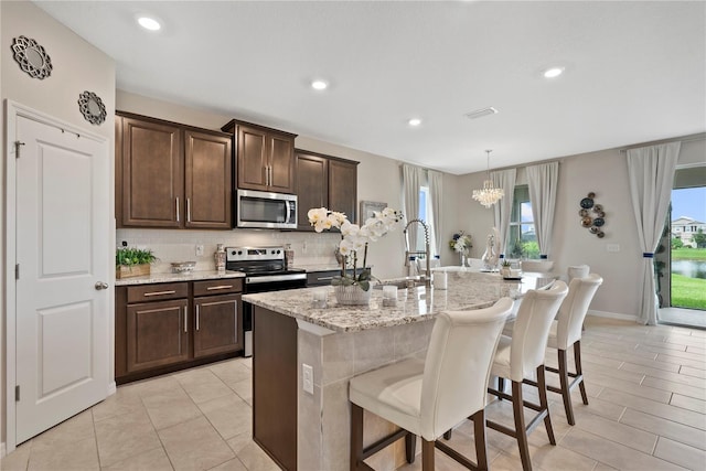 5313 Halewood Ct, Lakewood Ranch, FL 34211 - kitchen with appliances with stainless steel finishes, decorative backsplash, a chandelier, light stone countertops, and an island with sink