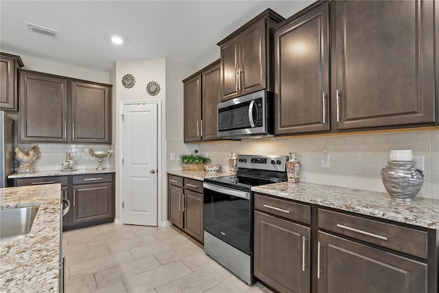 5313 Halewood Ct, Lakewood Ranch, FL 34211 - kitchen with stainless steel appliances, dark brown cabinetry, backsplash, light stone counters, and light tile patterned flooring