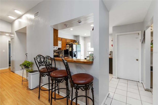 616 Bryan Terrace Dr, Brandon, FL 33511 - kitchen with brown cabinetry, black refrigerator with ice dispenser, a breakfast bar area, light wood-type flooring, and a peninsula