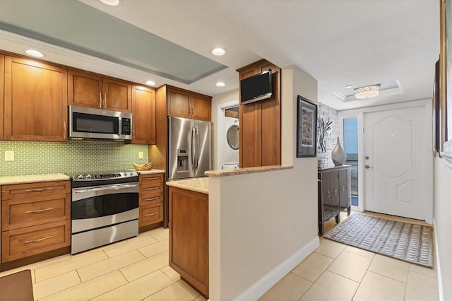 840 The Esplanade N Unit 805, Venice, FL 34285 - kitchen featuring stainless steel appliances, a raised ceiling, estacked washer and dryer, brown cabinetry, and light tile patterned flooring