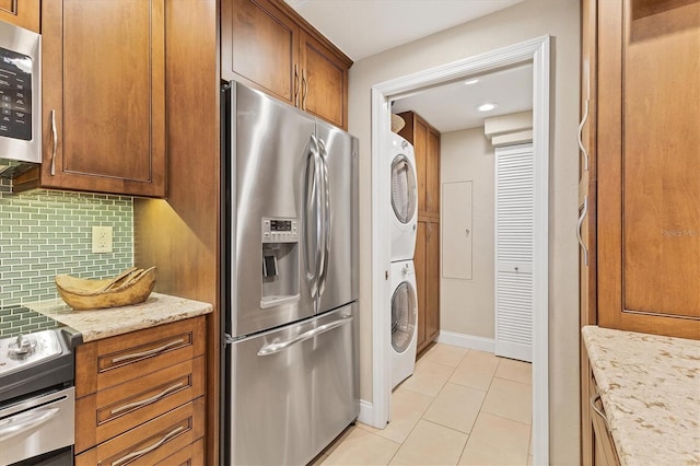 840 The Esplanade N Unit 805, Venice, FL 34285 - kitchen featuring stainless steel appliances, stacked washer and clothes dryer, backsplash, light tile patterned flooring, and brown cabinets