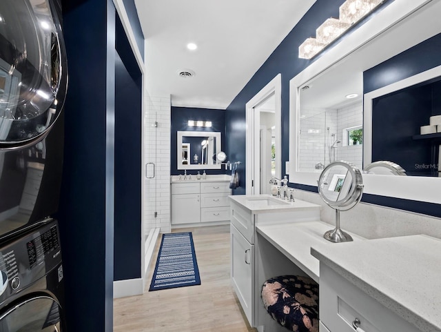 3439 Fair Oaks Pl, Sarasota, FL 34239 - full bathroom featuring stacked washing machine and dryer, a stall shower, two vanities, and wood finished floors