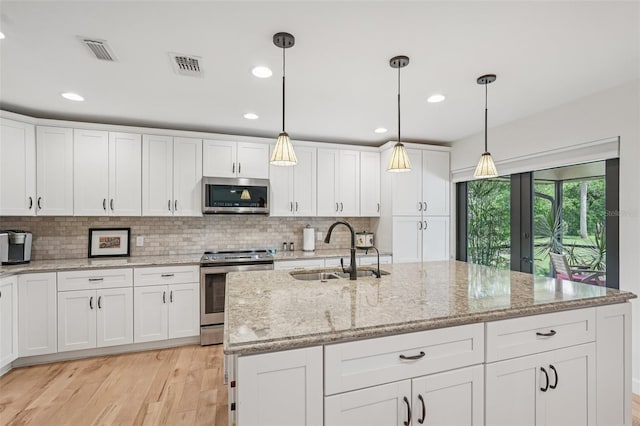5283 Everwood Run, Sarasota, FL 34235 - kitchen featuring appliances with stainless steel finishes, white cabinets, light wood-style flooring, backsplash, and a kitchen island with sink