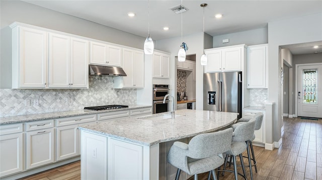 3431 Chestertown Loop, Bradenton, FL 34211 - kitchen with stainless steel appliances, under cabinet range hood, a center island with sink, backsplash, and white cabinets