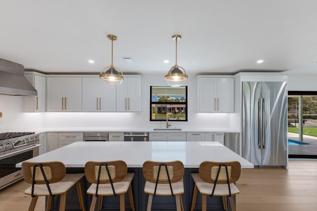510 Putter Ln, Longboat Key, FL 34228 - kitchen with appliances with stainless steel finishes, light countertops, light wood-type flooring, wall chimney exhaust hood, and a kitchen bar