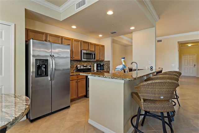 7121 River Hammock Dr Unit 102, Bradenton, FL 34212 - kitchen featuring stainless steel appliances, brown cabinetry, dark stone countertops, a breakfast bar, and light tile patterned flooring