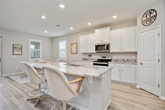 12357 Nantahala Run, Parrish, FL 34219 - kitchen with stainless steel appliances, an island with sink, white cabinets, light wood-type flooring, and a breakfast bar area