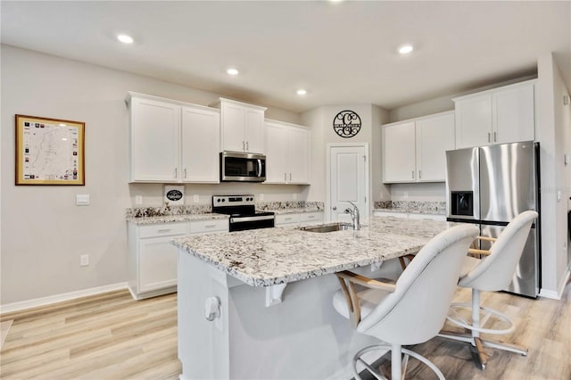 12357 Nantahala Run, Parrish, FL 34219 - kitchen with appliances with stainless steel finishes, a kitchen bar, white cabinetry, light wood finished floors, and recessed lighting