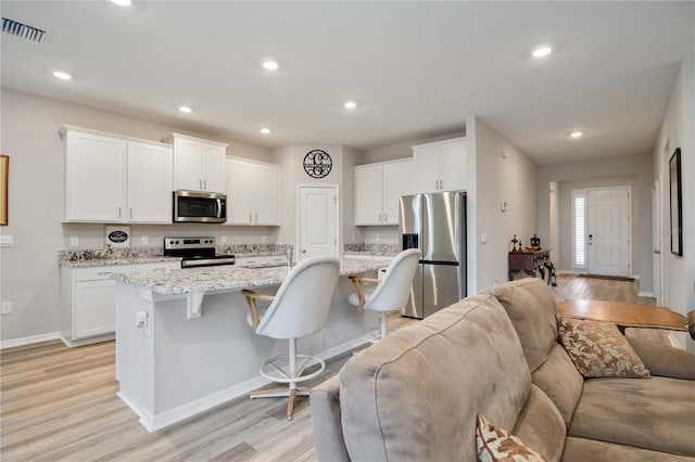 12357 Nantahala Run, Parrish, FL 34219 - kitchen featuring stainless steel appliances, a kitchen bar, light wood finished floors, open floor plan, and white cabinets
