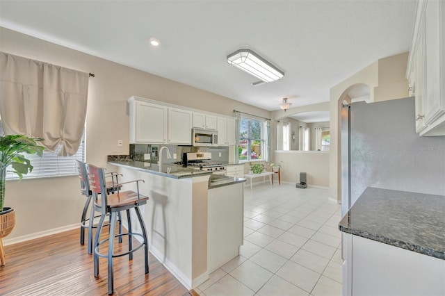14255 Gnatcatcher Ter, Lakewood Ranch, FL 34202 - kitchen with stainless steel microwave, gas stove, arched walkways, white cabinets, and a peninsula