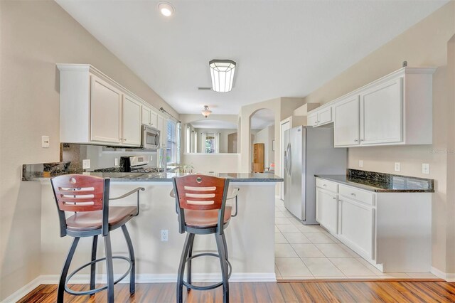 14255 Gnatcatcher Ter, Lakewood Ranch, FL 34202 - kitchen with appliances with stainless steel finishes, a peninsula, white cabinets, a kitchen bar, and arched walkways