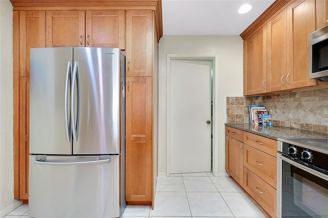 4339 Bowling Green Cir Unit 19, Sarasota, FL 34233 - kitchen featuring appliances with stainless steel finishes, backsplash, dark stone countertops, light tile patterned flooring, and brown cabinetry