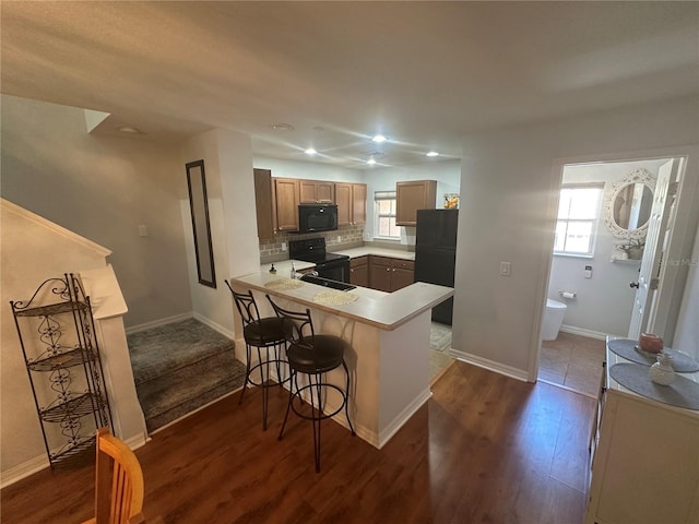 8809 White Sage Loop, Lakewood Ranch, FL 34202 - kitchen with black appliances, dark wood-type flooring, a kitchen breakfast bar, a peninsula, and decorative backsplash