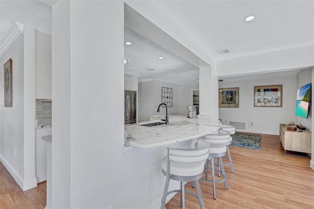 6962 Belgrave Dr, Sarasota, FL 34242 - kitchen with stainless steel fridge, a breakfast bar, light wood finished floors, light stone counters, and white cabinets