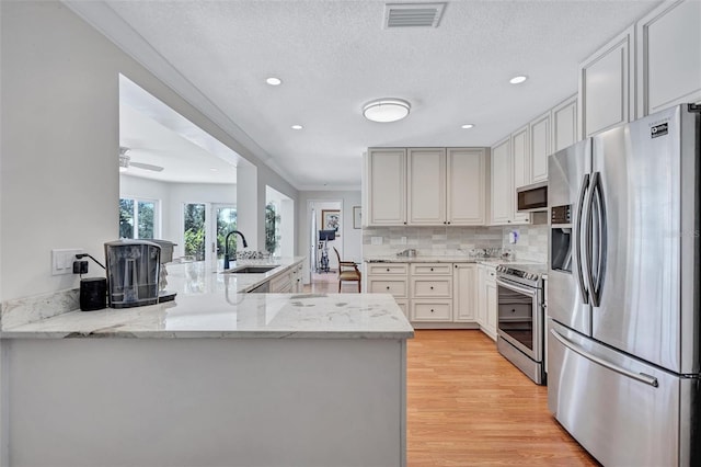 6962 Belgrave Dr, Sarasota, FL 34242 - kitchen with appliances with stainless steel finishes, light wood finished floors, decorative backsplash, light stone countertops, and a peninsula