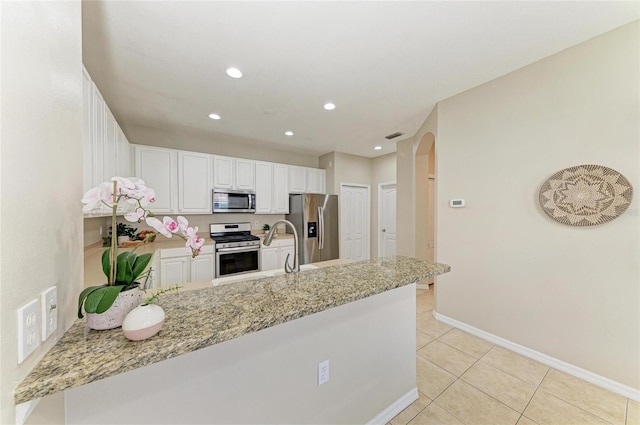 7039 Woodmore Ter, Lakewood Ranch, FL 34202 - kitchen featuring stainless steel appliances, a peninsula, arched walkways, light stone counters, and light tile patterned floors