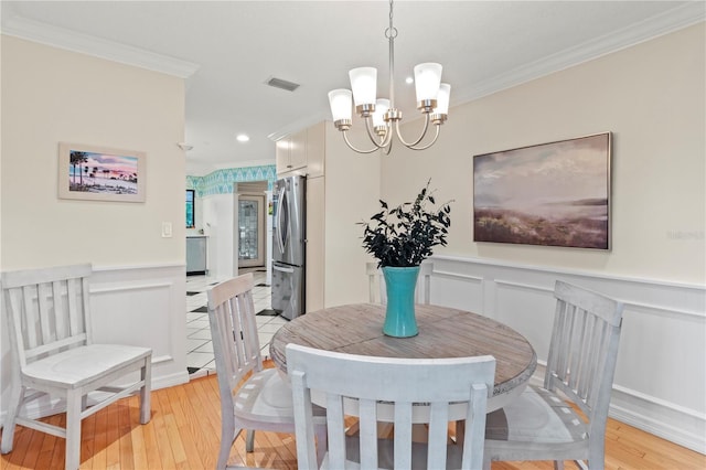 6818 Arbor Oaks Cir, Bradenton, FL 34209 - dining room featuring ornamental molding, a chandelier, light wood-style flooring, a wainscoted wall, and a decorative wall