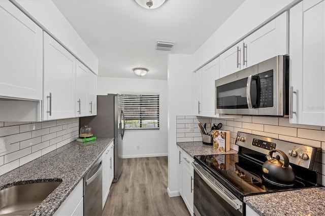 4658 Longwater Chase Unit 104, Sarasota, FL 34235 - kitchen with appliances with stainless steel finishes, backsplash, white cabinetry, and light wood-type flooring