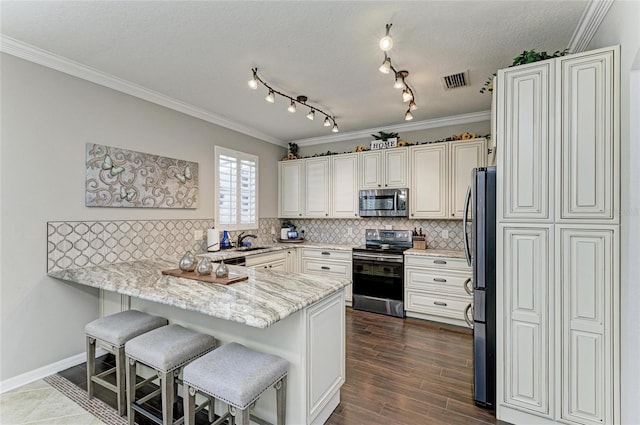 3911 91st Ave E, Parrish, FL 34219 - kitchen featuring appliances with stainless steel finishes, a peninsula, ornamental molding, a kitchen breakfast bar, and decorative backsplash
