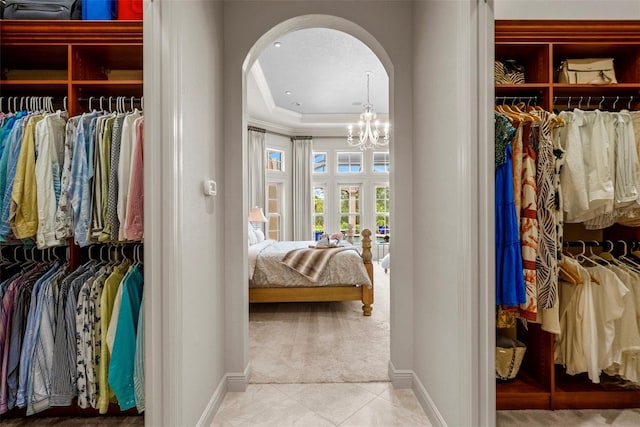 6926 Lacantera Cir, Lakewood Ranch, FL 34202 - walk in closet featuring arched walkways, carpet floors, a chandelier, tile patterned flooring, and a tray ceiling